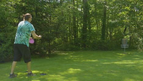 A-man-attempts-a-putt-towards-the-basket-in-a-wooded-disc-golf-course,-demonstrating-concentration-and-skill-in-the-sport