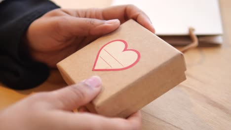hands holding a small gift box with a heart design