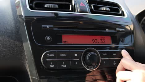 close up image of driver's hand press button on car radio, listening music during trip