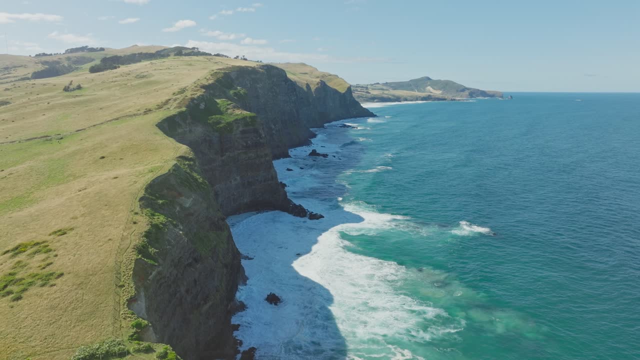 Dramatic aerial view over steep rocky cliffs and white wash ocean waves at Smails Beach on the Otago Peninsula, Dunedin, New Zealand Aotearoa