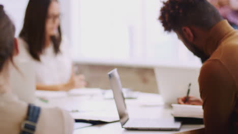 Millennial-black-woman-stands-presenting-to-colleagues-in-a-meeting,-tilt-shot,-rack-focus,-close-up