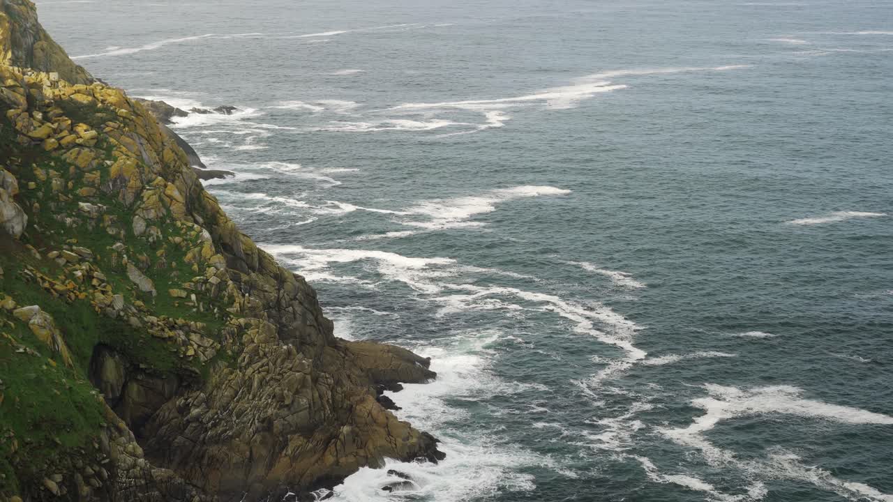 Static shot of a huge cliff with the sea eroding the rocks of the shore