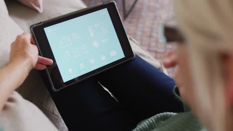 Happy-senior-caucasian-woman-sitting-on-sofa-in-living-room,-using-tablet