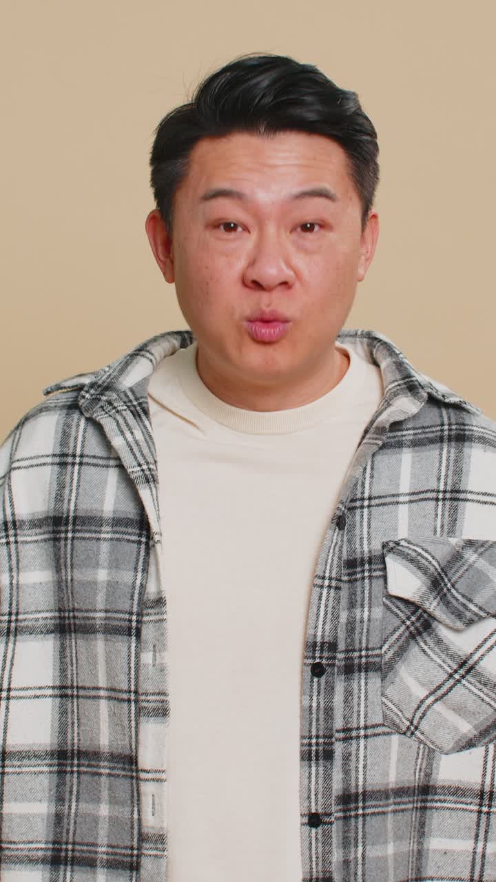 Asian mature man holds magnifying glass near face looking at camera with big zoomed eye analyzing