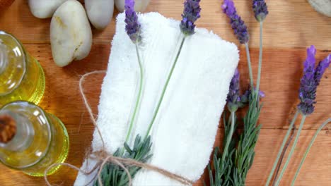 cuenco de madera con pétalos de lavanda, piedra de guijarros, botella de aceite y toalla