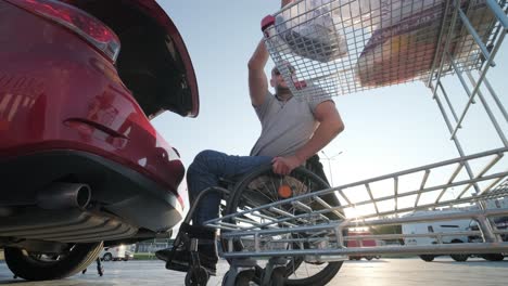 hombre adulto con discapacidad en silla de ruedas pone compras en el maletero de un coche en un estacionamiento de supermercado