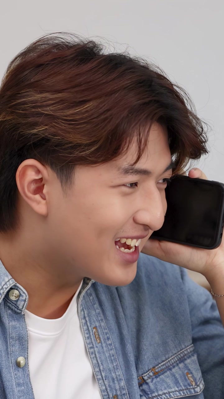 Primo piano del volto di un giovane uomo asiatico con una camicia di jeans che parla seriamente su uno smartphone.