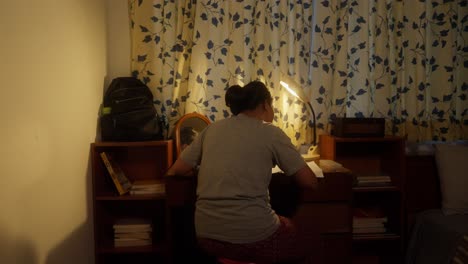 chica indonesia asiática estudiando escribiendo la tarea en el escritorio en una habitación con una cálida luz de tungsteno