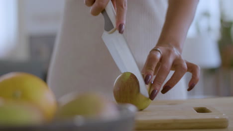 Closeup-of-female-hands-cutting-apple-on-wooden-board.