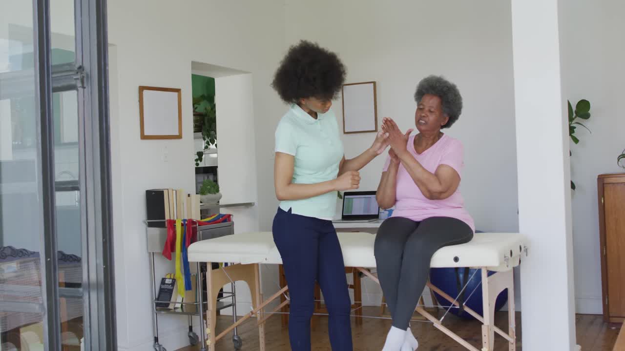 fisioterapeuta afroamericana que usa una máscara facial ayudando a una paciente anciana a hacer ejercicio