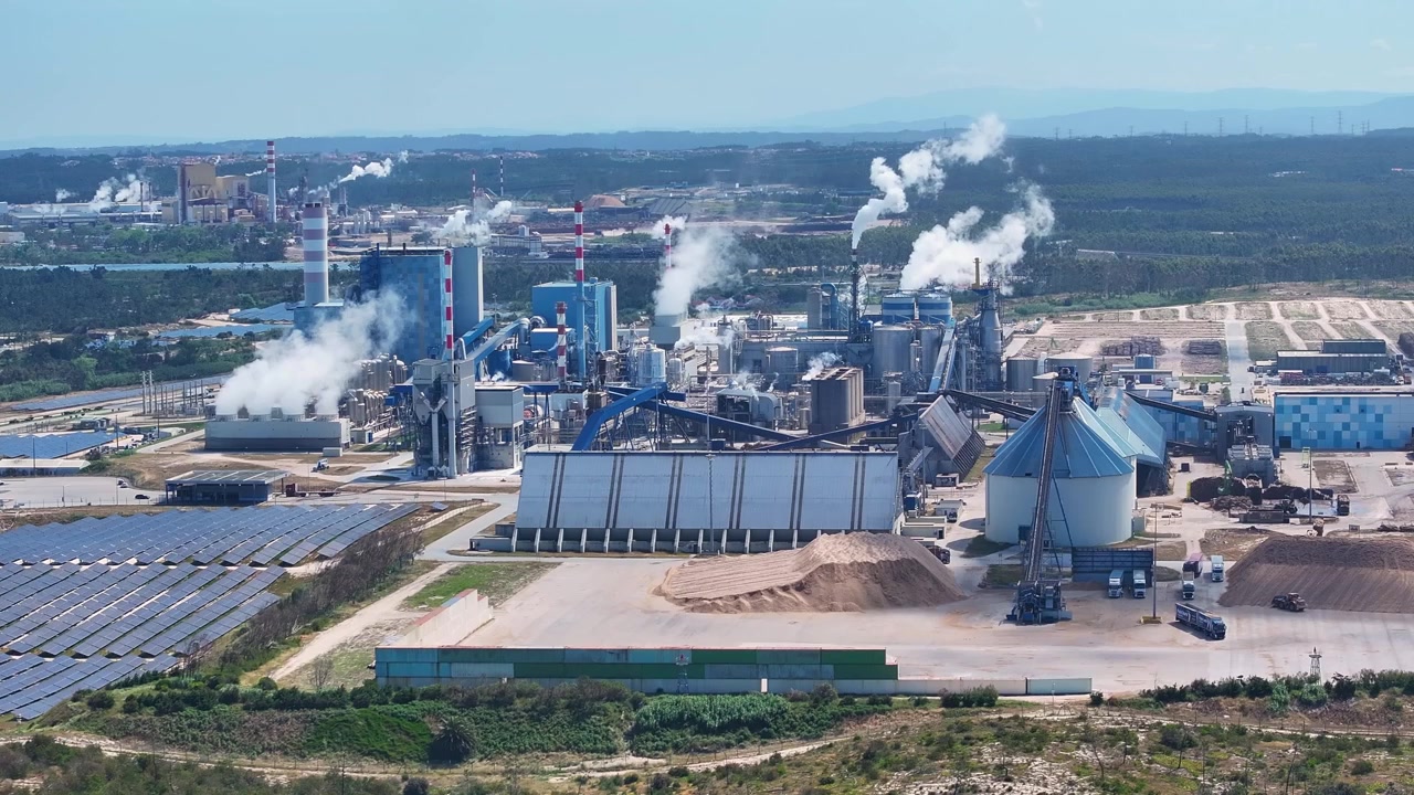Modern pulp and paper mill emitting steam from its smokestacks. Industrial complex includes a solar farm and biomass power plant for energy