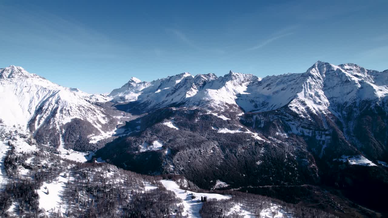 Vista aerea di un paesaggio montano innevato con foreste in una soleggiata giornata invernale ad Alp Grum, Svizzera