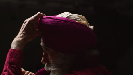 close up low key studio lighting shot of senior sikh man with beard using salai needle when putting on turban against dark background 1