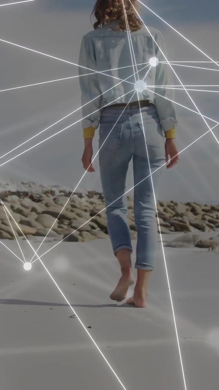 Vídeo vertical: Mulher caminhando na areia, com a câmera subindo e nós digitais se movendo sobre ela em direção às rochas, para tecnologia.