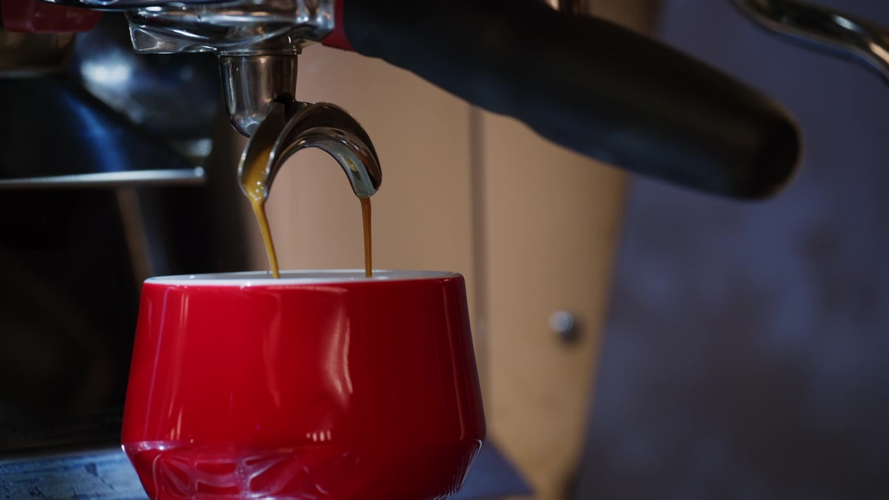 Caffè espresso fresco che scorre da una macchina da caffè professionale in una tazza di ceramica rossa.