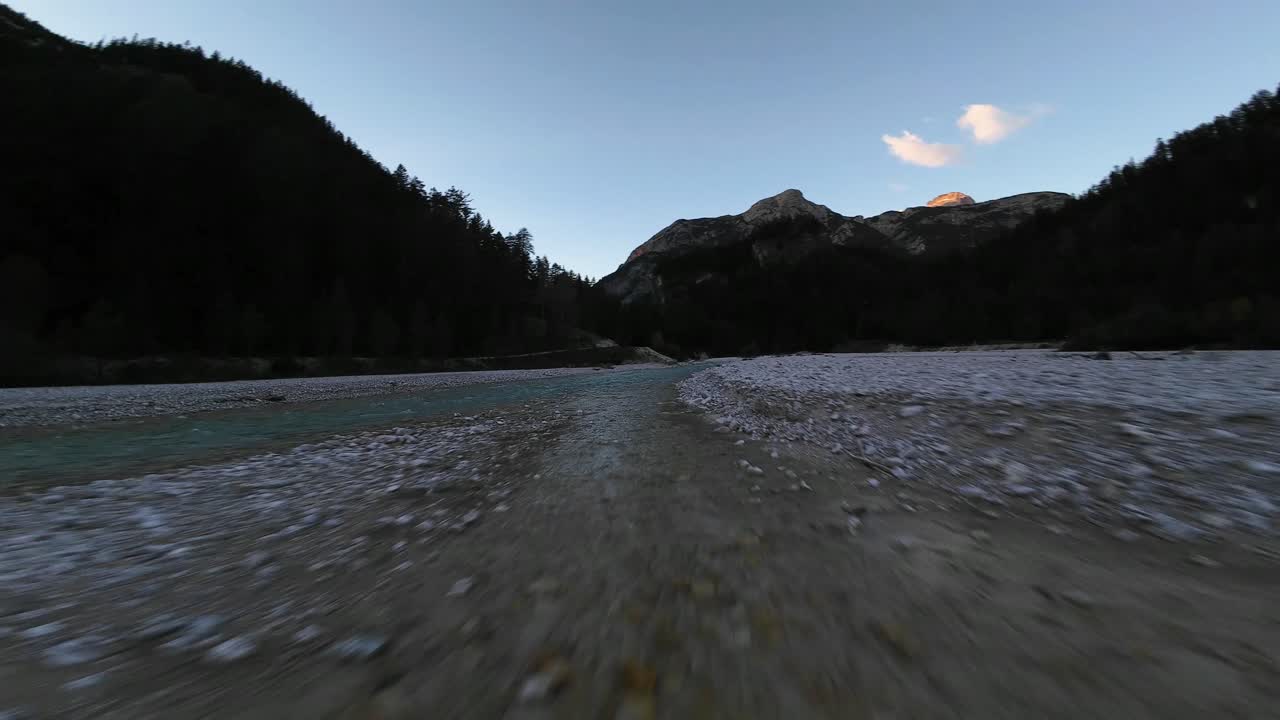 low flying aerial footage over a mountain riverbank in Switzerland at sunset dusk, with an adventurous, dynamic nature feel