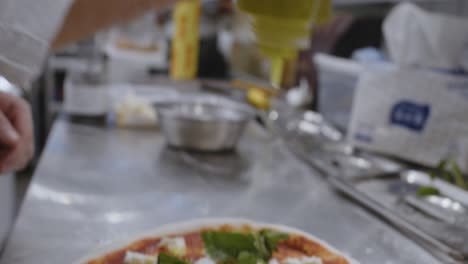 putting olive oil on top of neapolitan pizza on cooking table in pizzeria