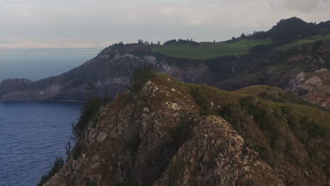 Aerial-orbit-around-jagged-sharp-cliff-with-sweeping-view-of-golf-course-off-in-distance