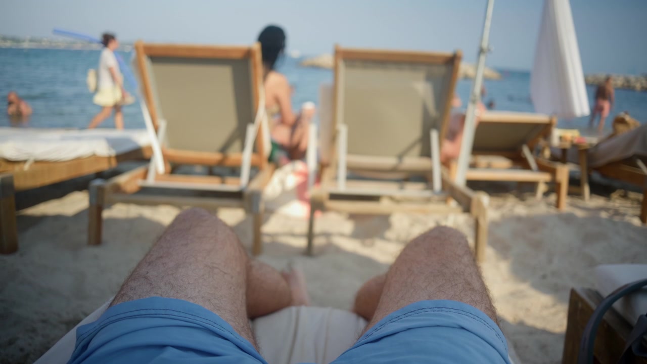 Vista in prima persona di una persona sdraiata su un lettino, che si sente rilassata su una spiaggia sabbiosa durante le vacanze estive.
