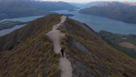 young caucasian woman running on a path along a mountain ridge to a viewpoint at roy's peak, wanaka, new zealand.