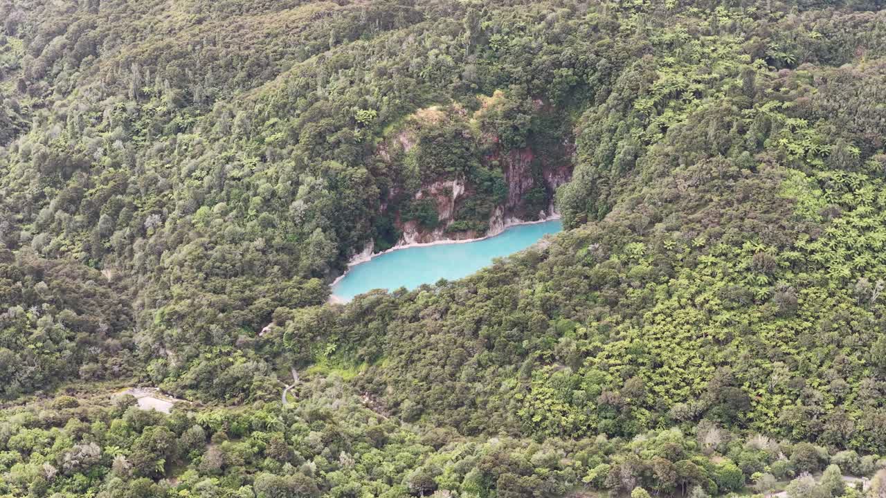 Dronebane med klokken rundt en turkis kratersjø i Waimangu vulkandal, New Zealand, med geotermiske trekk og filmatisk landskapsutsikt.