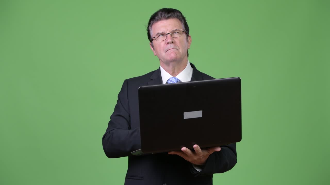 Senior handsome businessman thinking while using laptop