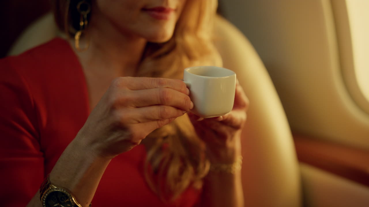 Primer plano de rubia bebiendo café durante viaje en avión. Dama elegante disfrutando.