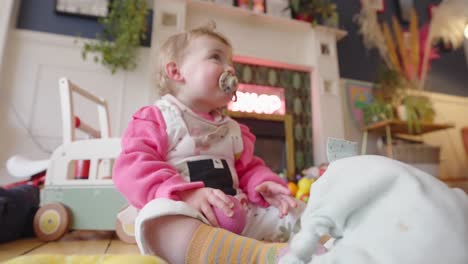 Toddler-enjoying-playing-with-pink-ball-and-her-soother-in-family-home