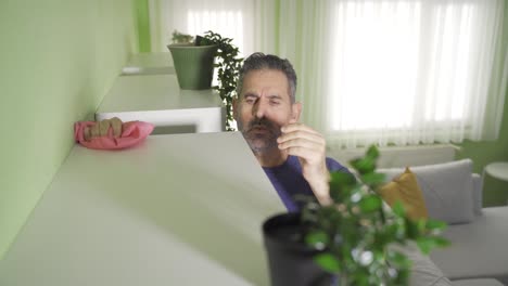 limpieza del hogar. un hombre de mediana edad vestido casualmente limpia los estantes de la suciedad usando un aspirador.
