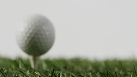 close up of golf tee and ball on grass and white background, copy space, slow motion