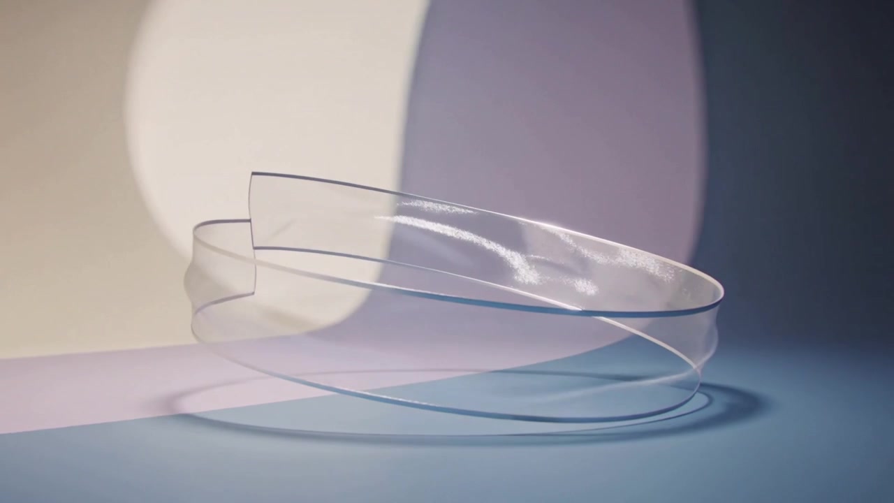 Tilting clear loop rotating and settling above pale blue table with cream backdrop, casting shadow