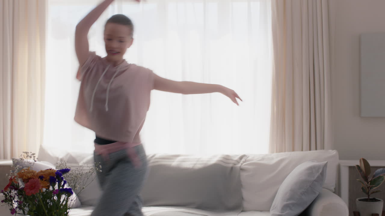 아름다운 십대 소녀가 집에서 춤을 추고 발레 댄스 동작을 연습하고 거실에서 재미있게 연습하고 있습니다.