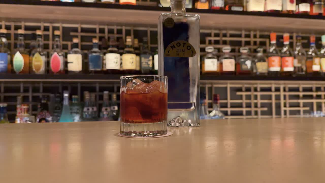 Uno zoom all'indietro lento rivela un cocktail Negroni e una bottiglia su un bancone di legno.