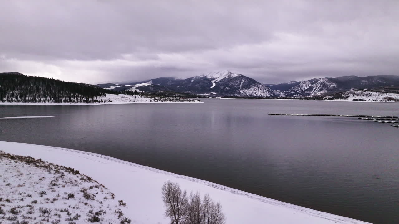 Elokuvamainen drone-ilmakuva Dillonjärvestä, Keystone Summit Covesta, Coloradosta. Pilvinen, luminen talviaamunäkymä Friscoon, Breckenridgeen, Silverthorneen ja Ten Mile Range -vuoristoon. Rauhallinen ja tyyni, jäätynyt maisema paljastuu eteenpäin liikkuvassa kuvassa.