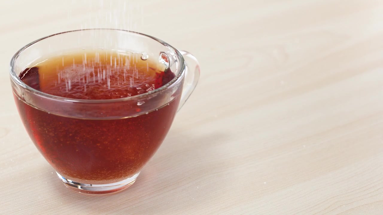 熱い紅茶が入った透明なガラスのカップに、白いグラニュー糖が注ぎ込まれる様子