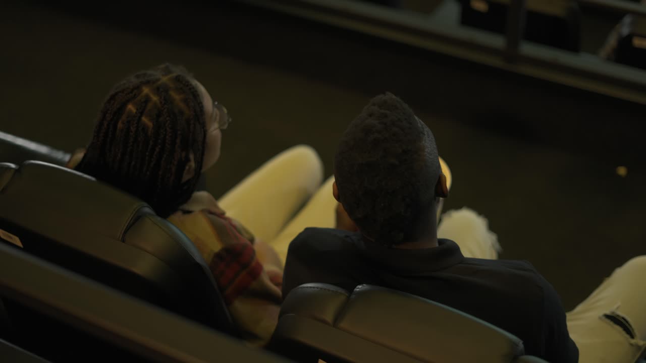 아프리카계 미국인 젊은 부부는 영화관에 와서 영화를 보고, 버에서 팝콘을 꺼내고, 위쪽을 바라보았다.