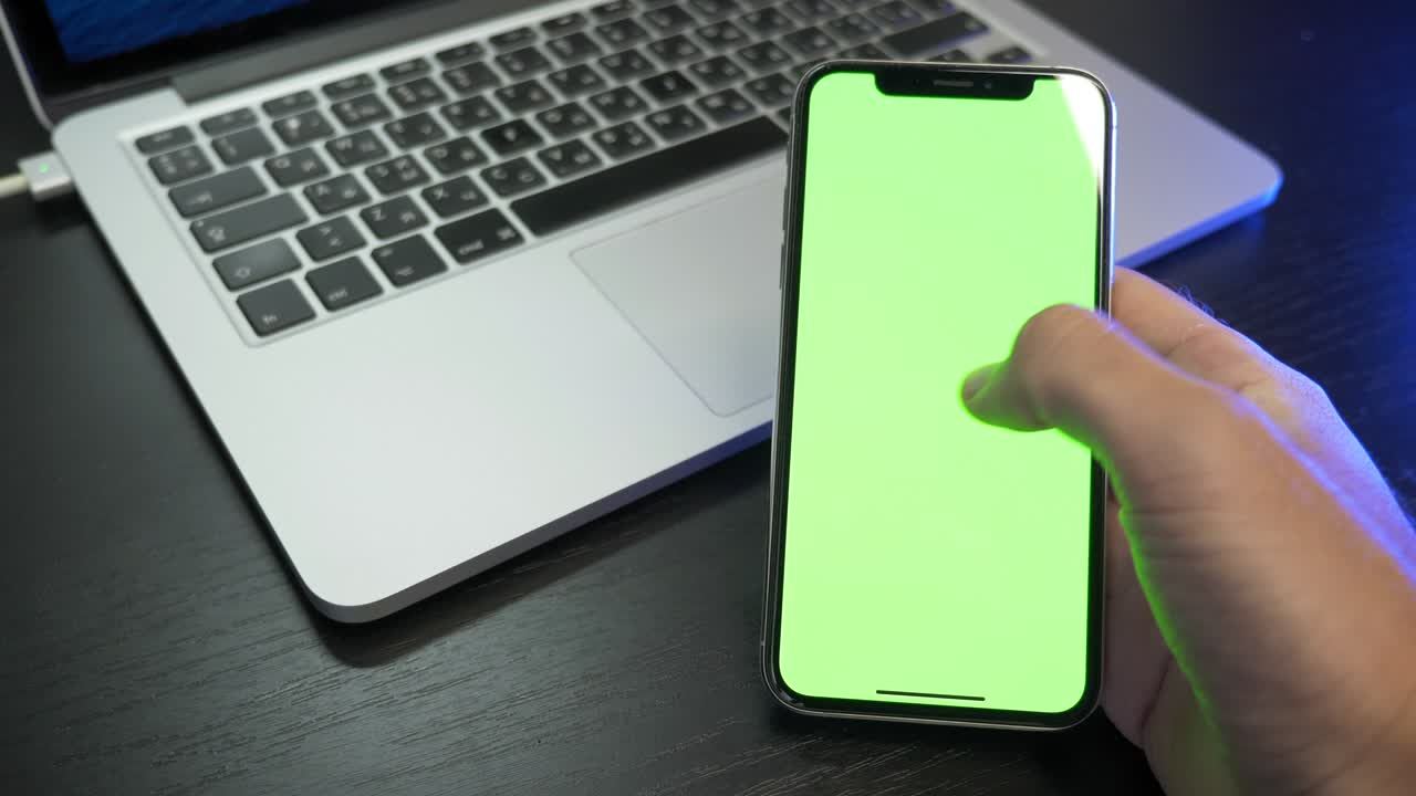 teléfono inteligente digital en blanco en la mano masculina. el hombre está sentado en la oficina y usando el teléfono con pantalla de maqueta verde, navegando por internet, viendo videos de contenido, desplazando noticias y tocando en la pantalla central