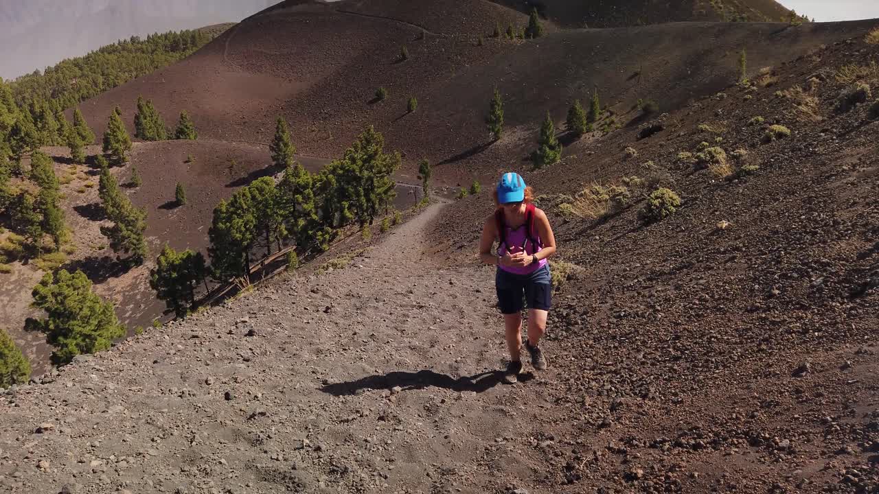 una foto de una mujer escalando un sendero polvoriento en un terreno volcánico