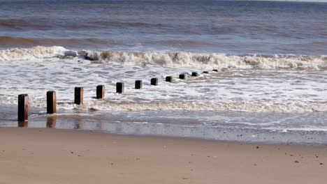 Waves-crashing-in-to-groynes-on-Skegness-beach,-wide-shot