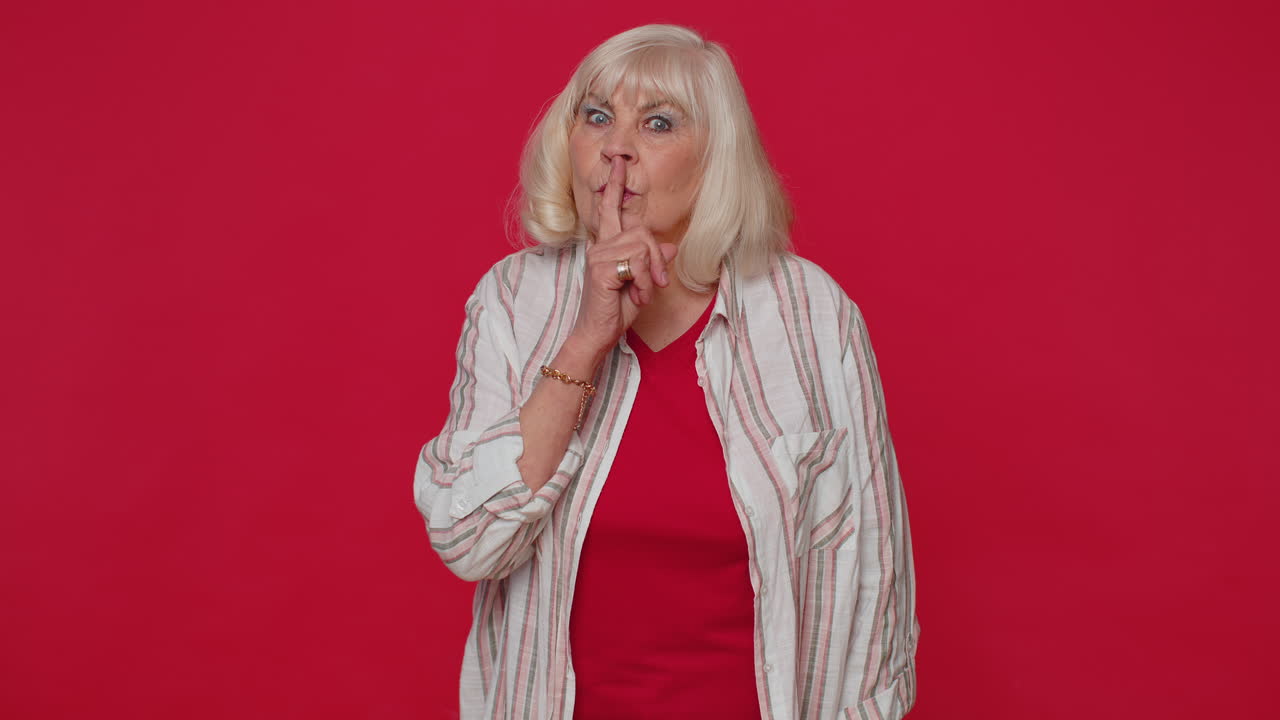 Mujer mayor se lleva el dedo índice a los labios haciendo un gesto de silencio, indicando que no se cuente un secreto, shh, guarda silencio.
