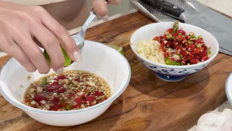 A person squeezes fresh lime juice into a bowl of Thai chili fish sauce mixture on a wooden countertop, under bright indoor lighting with a steady close-up camera angle