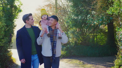 family with two dads on walk in winter countryside carrying daughter on shoulders