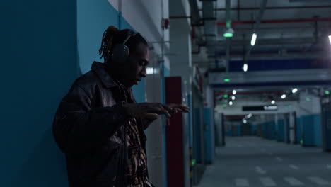 músico afroamericano rapero negro, con auriculares en el estacionamiento subterráneo, hace movimientos geniales al ritmo de la música en sus auriculares