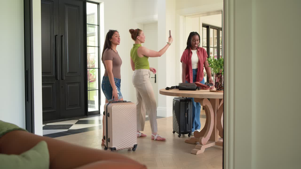 African American friends entering black doors, filming home with phone while placing suitcases