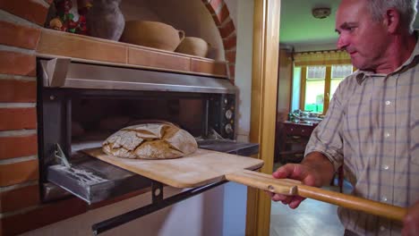 old baker man taking fresh delicious bread from old fashioned oven, medium shot