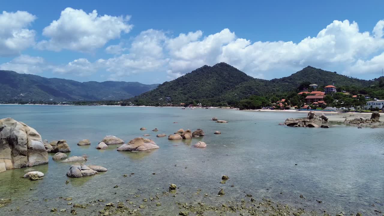 Aerial drone footage of Lamai Beach, Koh Samui, Thailand, showcasing rocky coastline, turquoise ocean water, lush green mountains, and scenic tropical island horizon under a clear sky