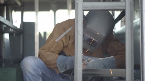 young male is welding metal object and taking off mask to check