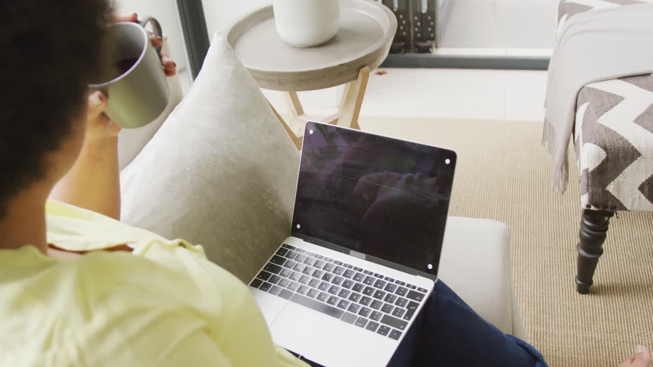 Video of plus size african american woman sitting on sofa with laptop with copy space