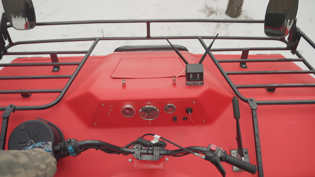 POV-fører sjekker rød ATV-kontroller før kjøring, hender justerer gass og brems, nærbilde av dashbordmålere synlig, hvit hjelm, inspeksjonsrutine i snødekt terreng, rolig, fokusert forberedelse.