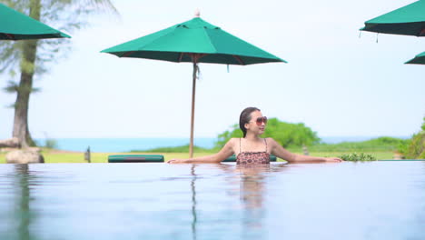 Mujer-Asiática-Sentada-En-La-Piscina-Con-Fondo-Tropical